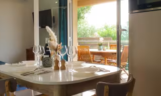Coin repas d'une mini-villa, table dressée devant la baie vitrée ouverte sur la terrasse