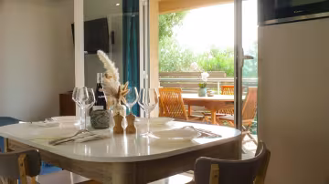 Coin repas d'une mini-villa, table dressée devant la baie vitrée ouverte sur la terrasse